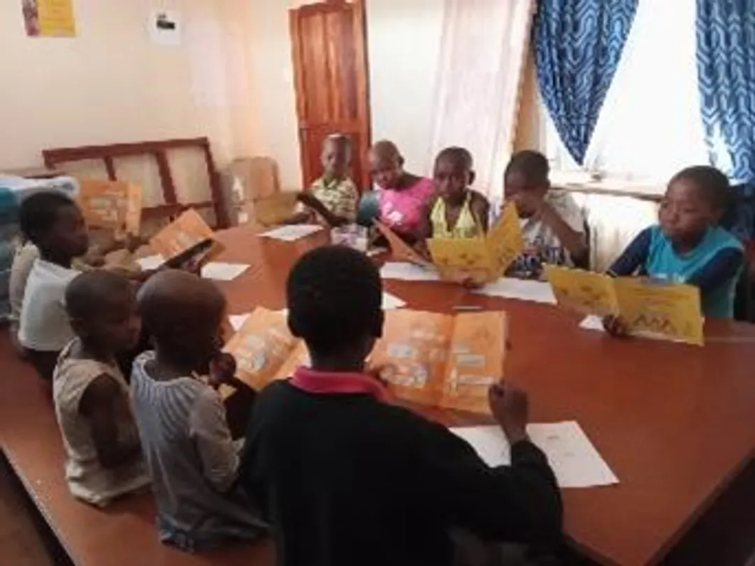 Children sitting around a table. All of the children are reading the same yellow book.